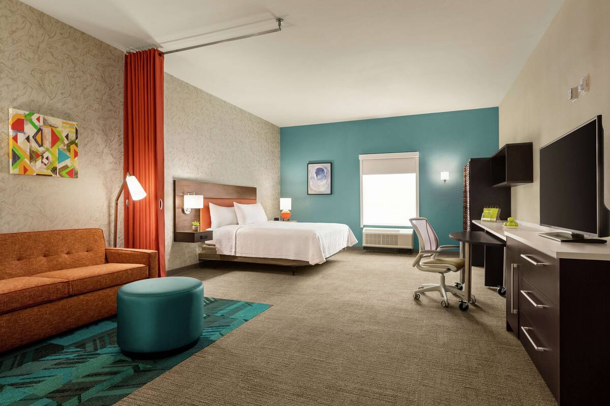 A hotel room with a bed, a sofa, a desk with a TV, a chair, and a window.
