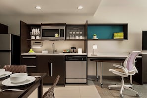 Une cuisine moderne avec des meubles de couleur sombre, un four à micro-ondes encastré, un lave-vaisselle et un coin repas comprenant une table et des chaises.
