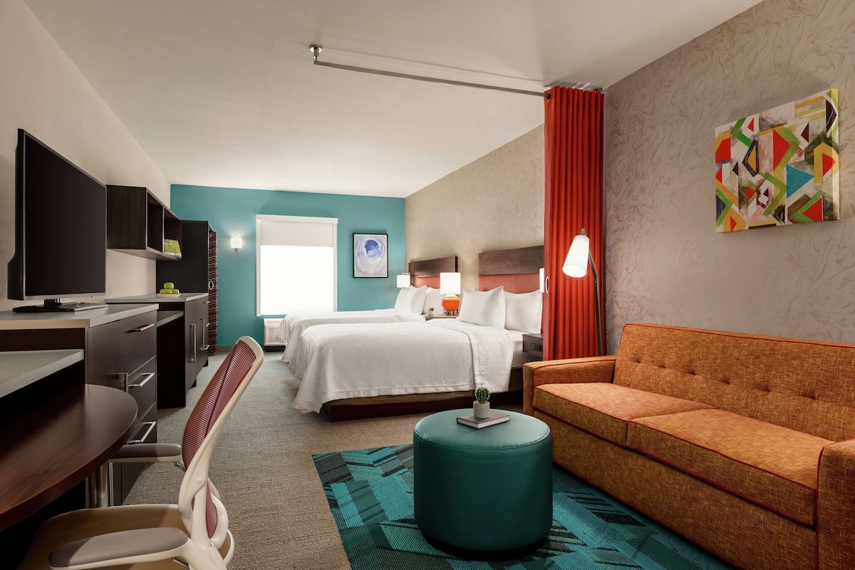 A hotel room with a bed, a desk, a chair, a sofa, and a television.