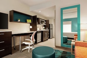 Une cuisine moderne équipée d’un four à micro-ondes, d’une cuisinière et de placards. On y trouve un bureau avec une chaise, ainsi qu’une petite table avec une lampe.
