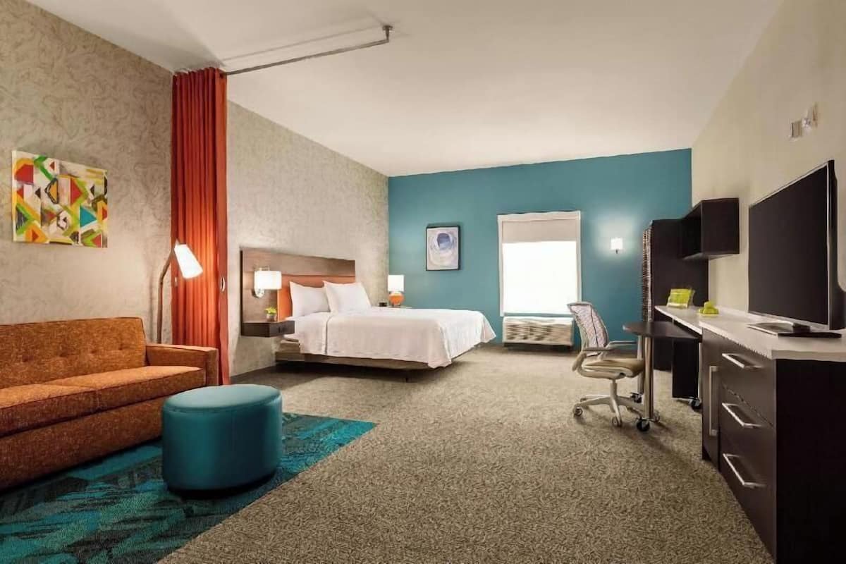 A hotel room with a bed, a desk, a chair, a sofa, and a television.
