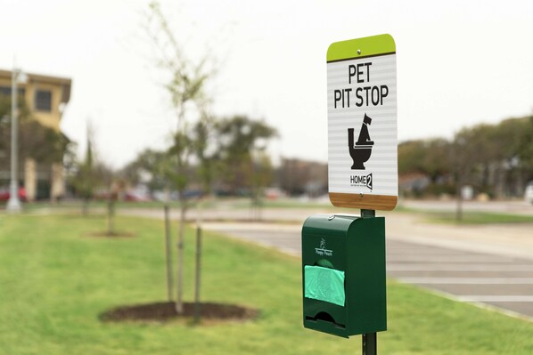 Un panneau indiquant un espace de repos pour animaux de compagnie, avec une poubelle et un conteneur à déchets vert.