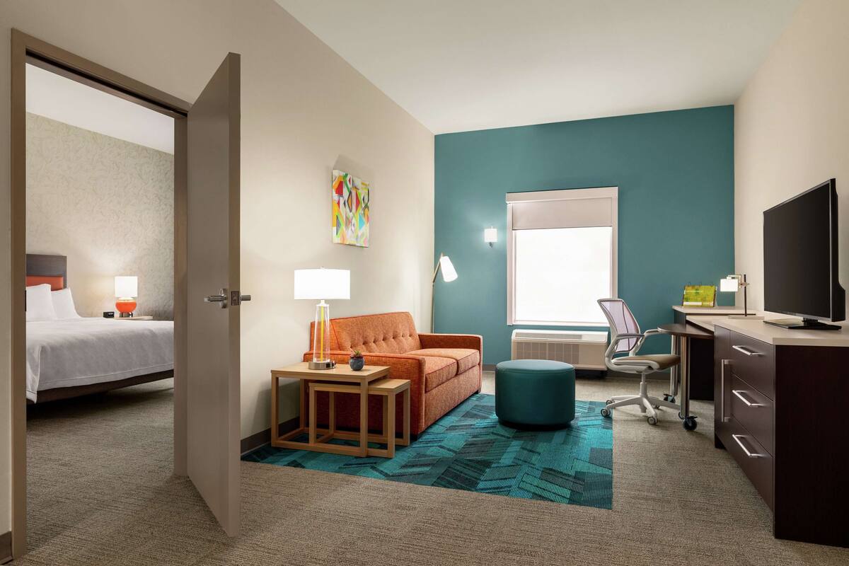 A hotel room with a bed, a sofa, a desk, a chair, and a TV.
