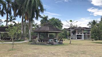 A gazebo in a grassy area with palm trees and a two-story building in the background.