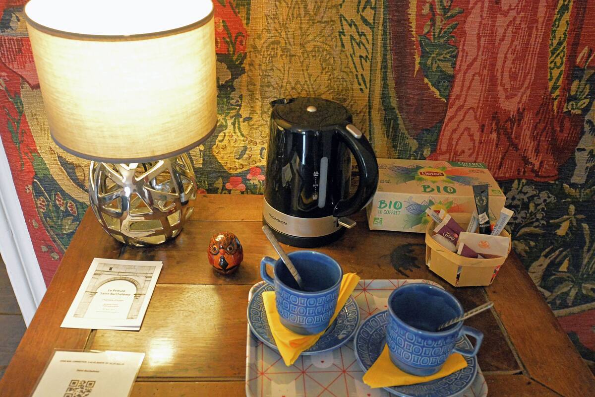 Une table avec une lampe, une bouilloire, un plateau avec des tasses et des soucoupes, une petite chouette décorative et une boîte de thé Lipton.