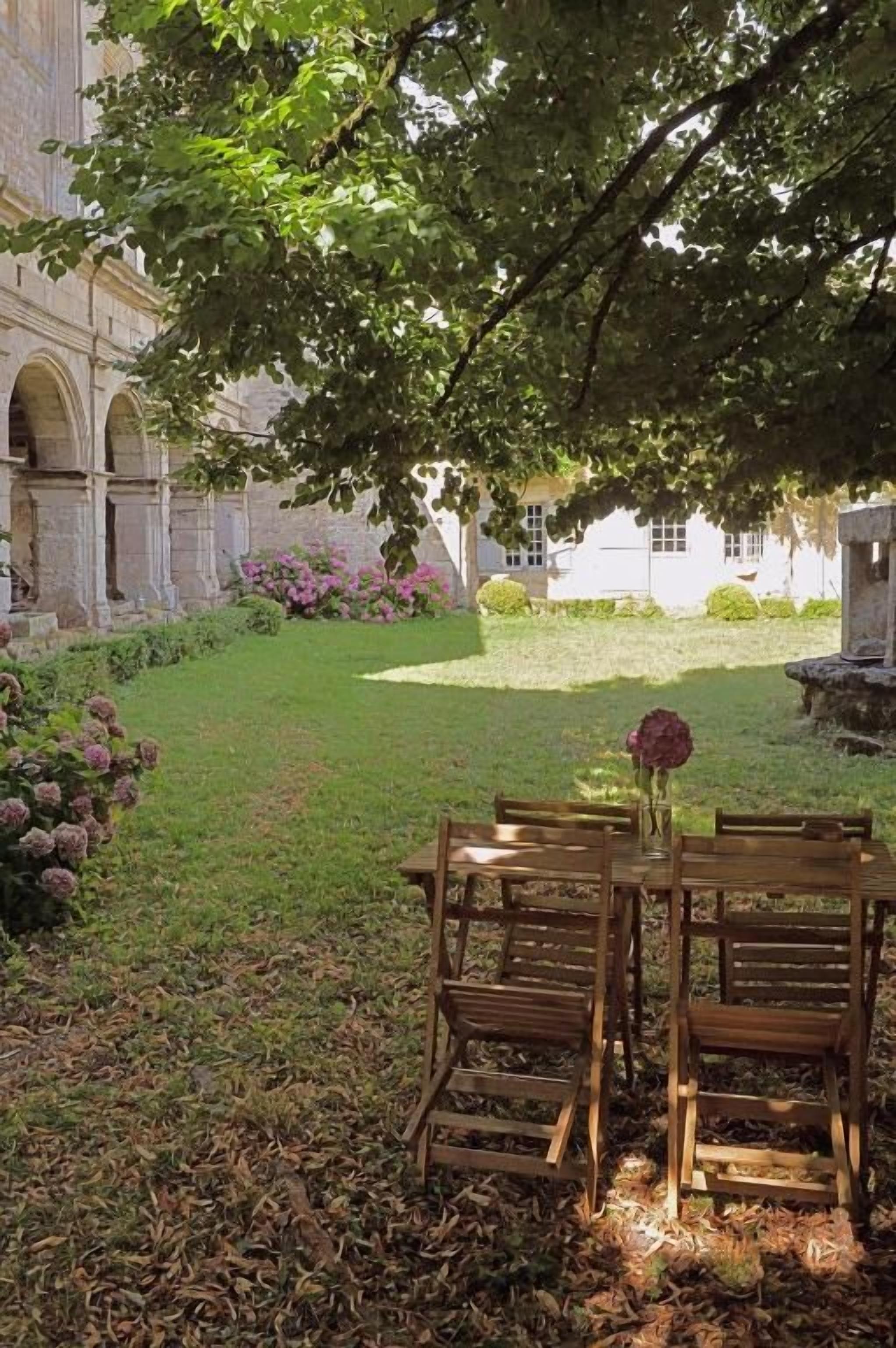An outdoor seating area with a table and chairs, surrounded by a garden with flowers and a building in the background.