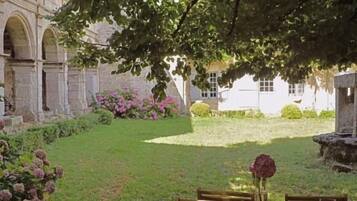 An outdoor seating area with a table and chairs, surrounded by a garden with flowers and a building in the background.
