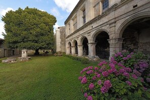 A historic building with a courtyard, stone arches, and a large tree.