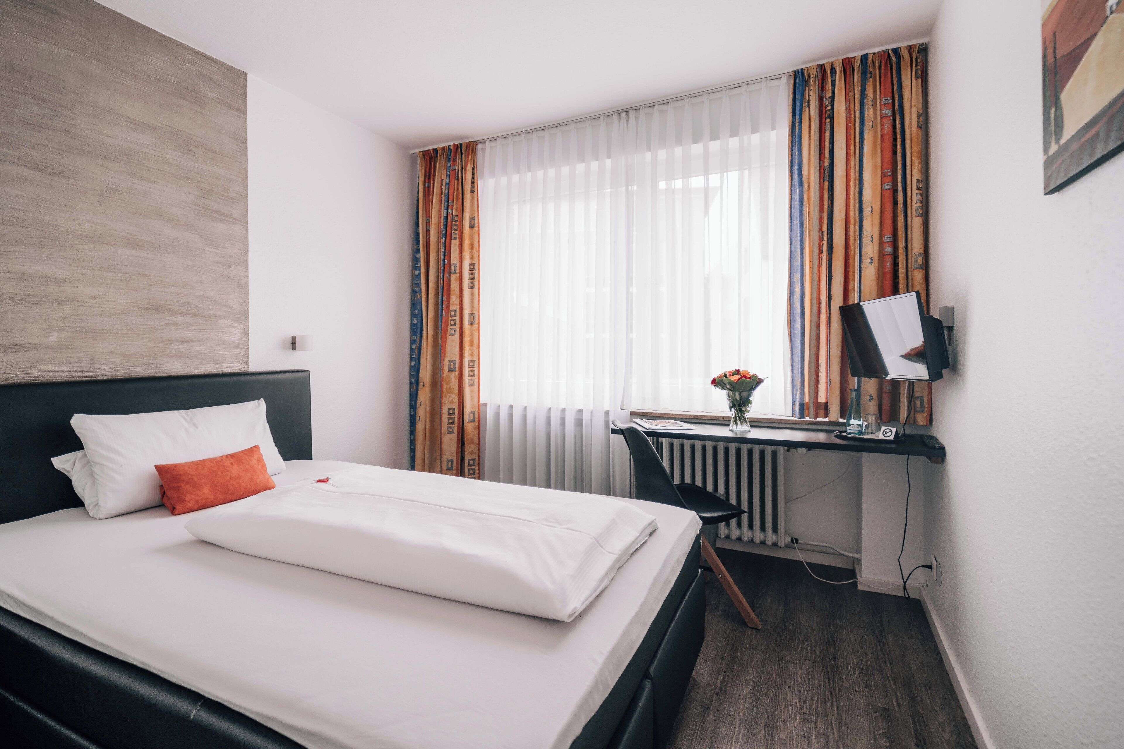 A hotel room with a bed, a desk, and a radiator.