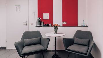 Una stanza con due poltrone grigie, un piccolo tavolo bianco con un vaso di fiori e un muro rosso e bianco.