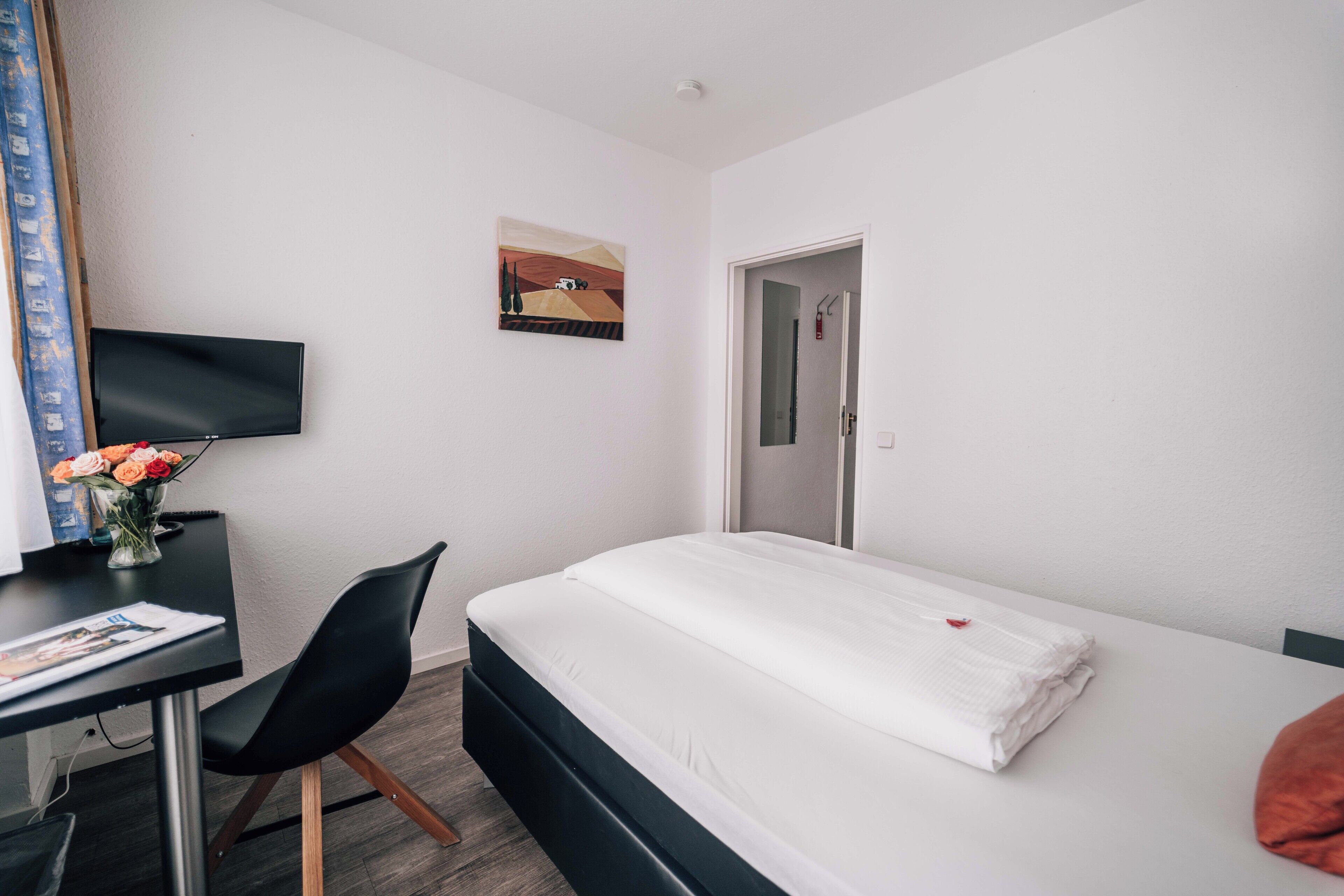 A hotel room with a bed, a desk with a chair, a television, and a painting on the wall.