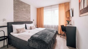 Une chambre d’hôtel moderne, dotée d’un grand lit, d’un bureau, d’une chaise et d’un téléviseur fixé au mur.