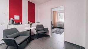 Un salon moderne avec deux fauteuils gris, une petite table ronde et un mur d’accent rouge.