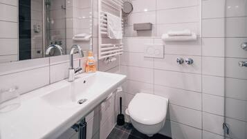 Ein modernes Badezimmer mit Waschbecken, Spiegel und Toilette in Weiß. Weiße Handtücher und ein Händetrockner sind an der Wand angebracht.