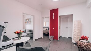 Une chambre d’hôtel moderne avec un coin repas, un mur d’accent rouge et une petite table agrémentée de fleurs.