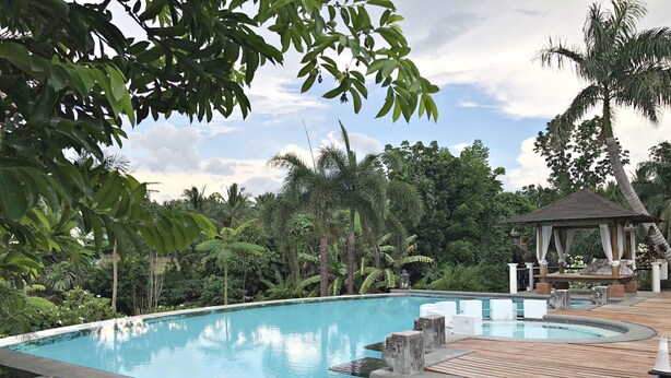 A pool area with a wooden deck, a gazebo, and lush greenery.