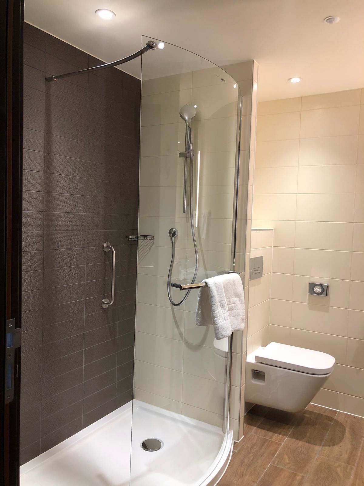 Un baño moderno con ducha de vidrio, inodoro blanco y una toalla colgada en un perchero.