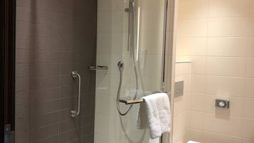 Un baño moderno con ducha de vidrio, inodoro blanco y una toalla colgada en un perchero.
