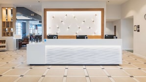 Un espace d’accueil d’hôtel au design moderne, comprenant un grand comptoir de réception, un luminaire fixé au mur et une signalétique bien visible indiquant l’emplacement des toilettes.