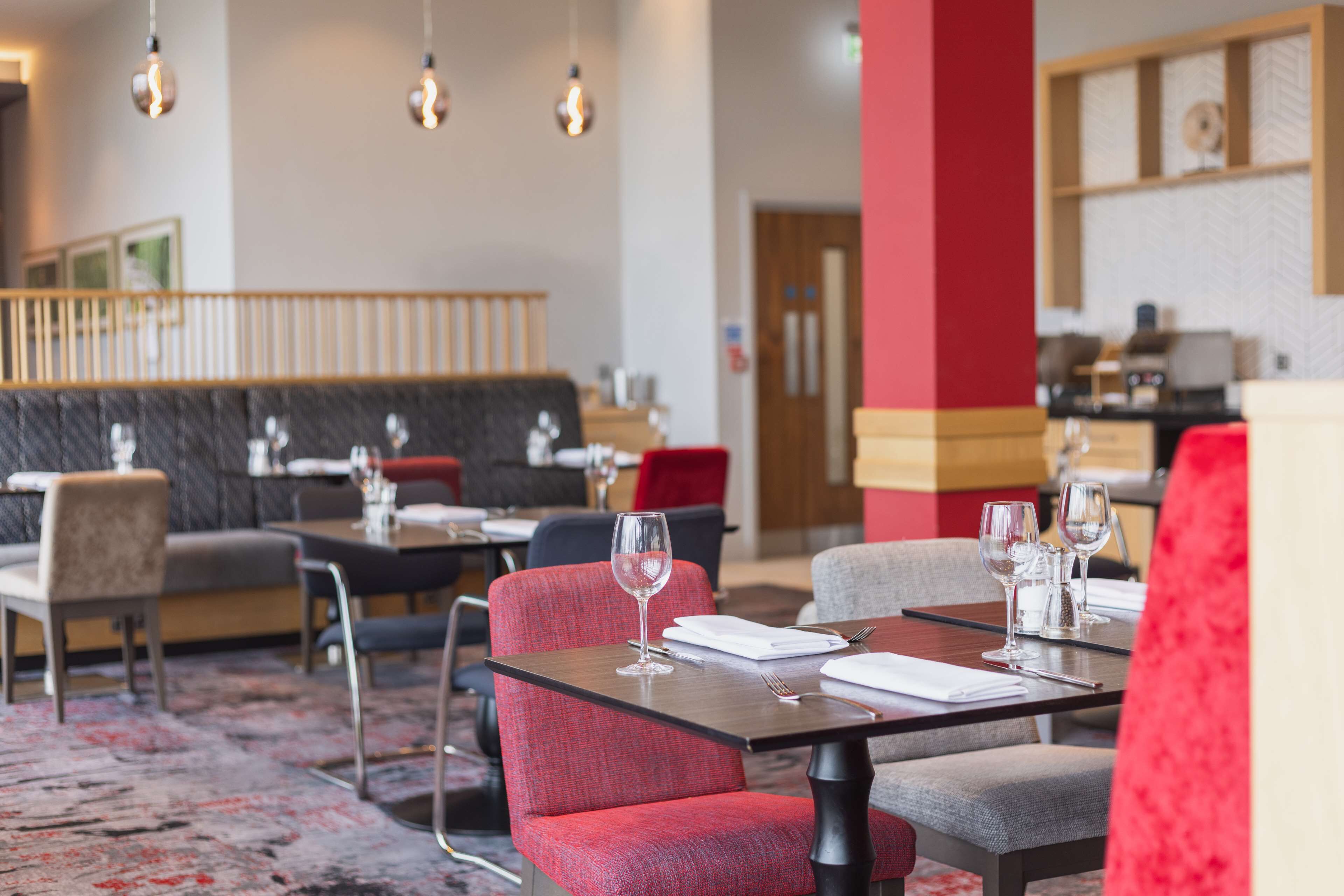 A restaurant with red and grey upholstered chairs, a black cushioned bench, and a wooden table with a wine glass and napkin.