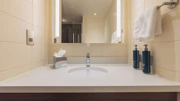 Une salle de bain moderne avec un lavabo blanc, un miroir, un porte-serviettes et deux flacons de produits de toilette.