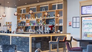 Un espace bar doté d’un comptoir en marbre, de plusieurs options d’assises et d’une variété de bouteilles et de verres exposés sur des étagères.
