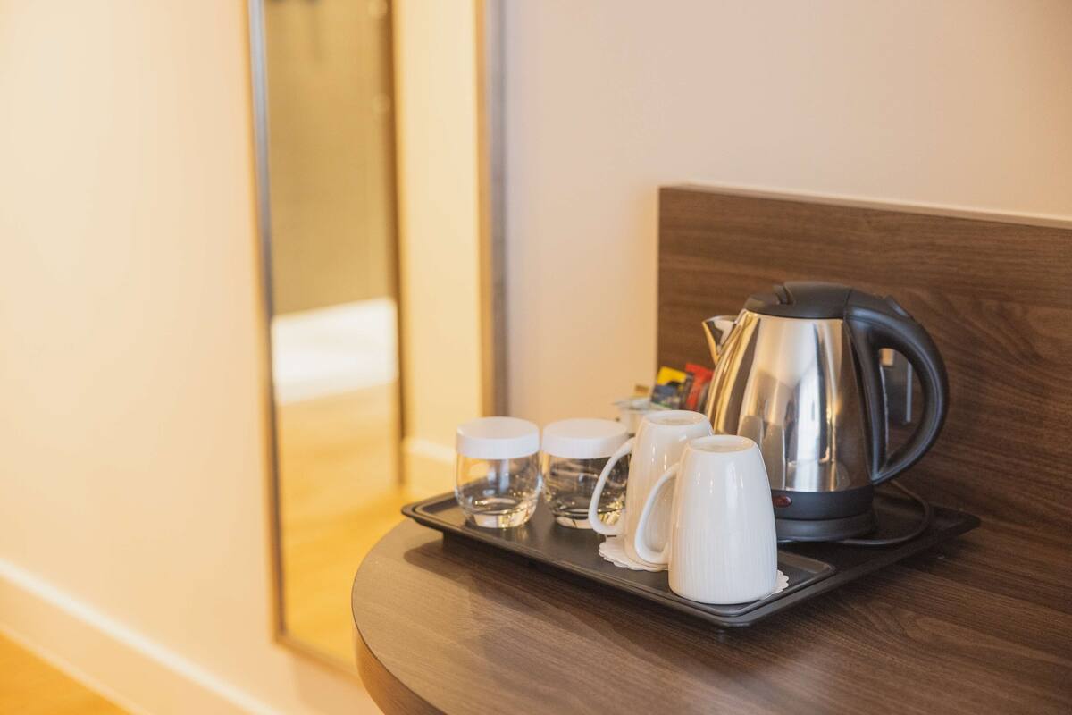 A tray with a kettle, two glasses, and two cups on a wooden surface.