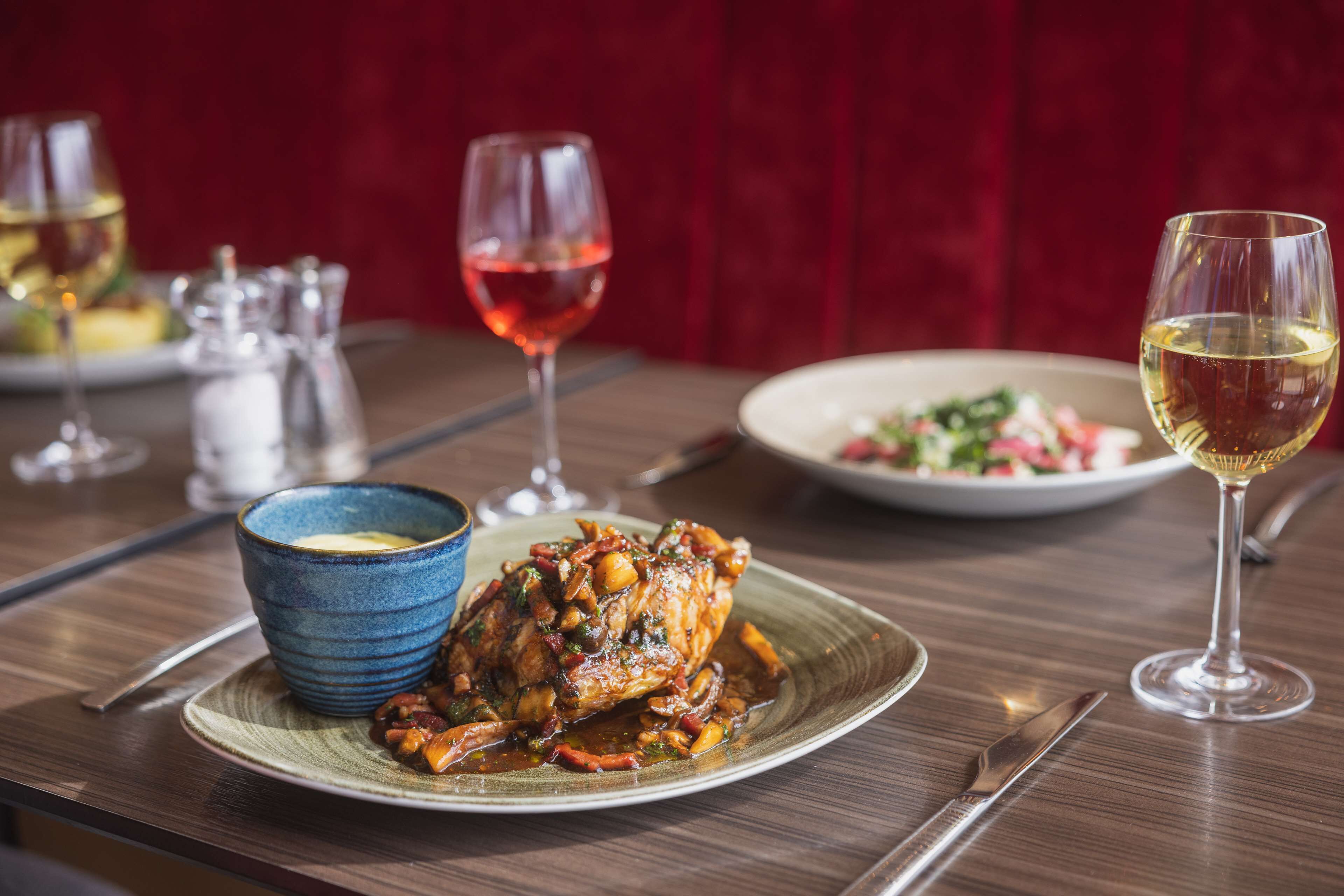 Una mesa de comedor con un plato de comida, un bol y dos copas de vino.