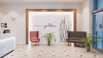 A reception area with a reception desk, two chairs, a wall with a welcome sign, and potted plants.