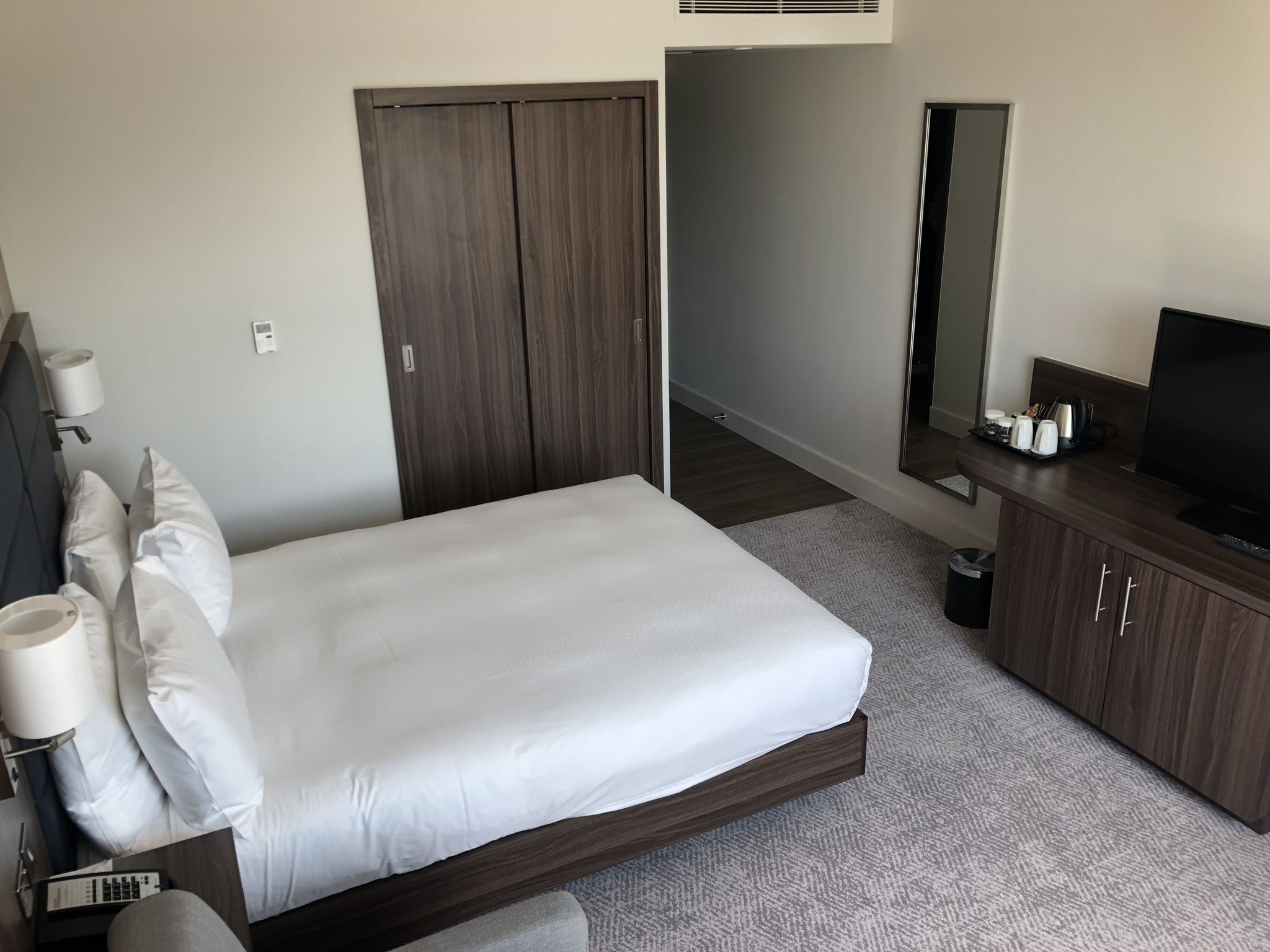 Habitación de hotel con cama, televisor, espejo y un mueble pequeño.