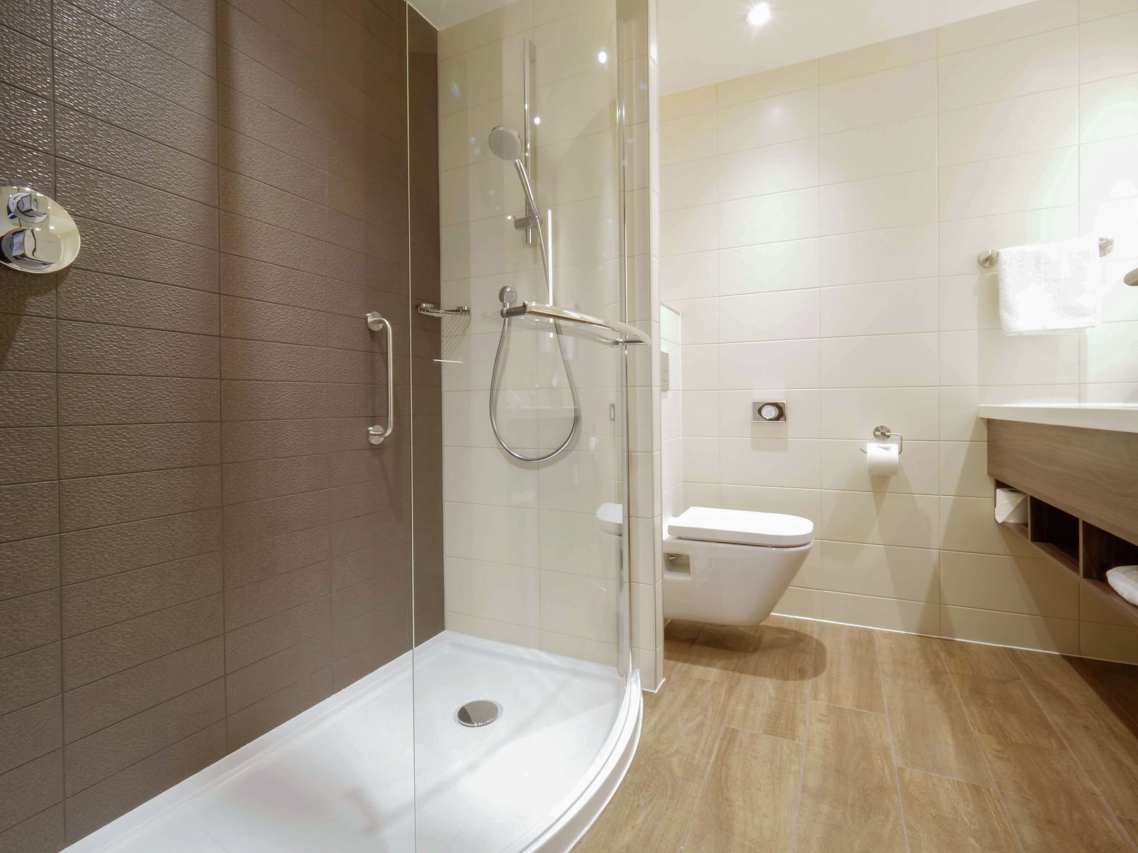 A modern bathroom with a glass-enclosed shower, a white toilet, and a wooden vanity.