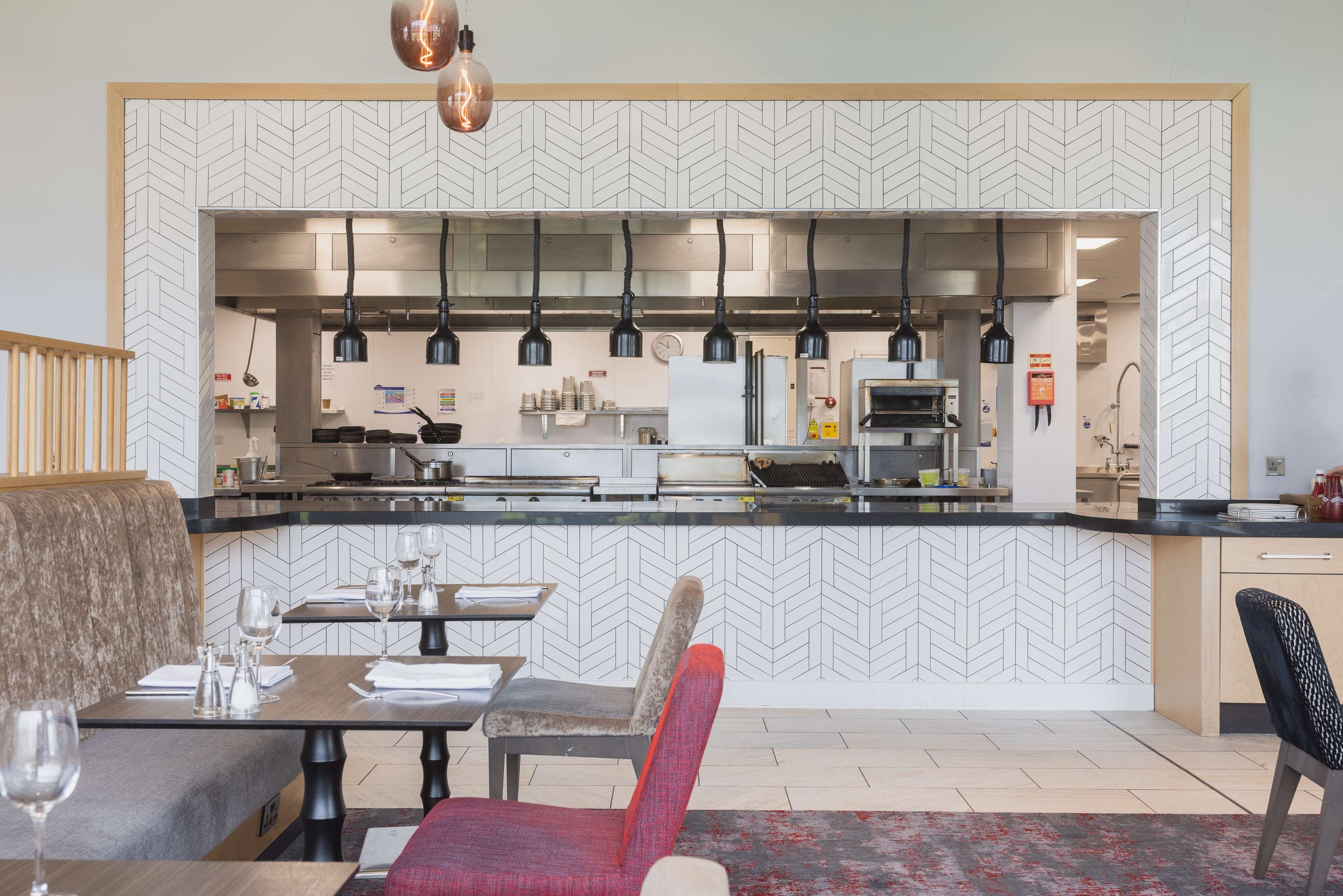 A modern restaurant with a herringbone-patterned wall, black pendant lights, and a central counter.