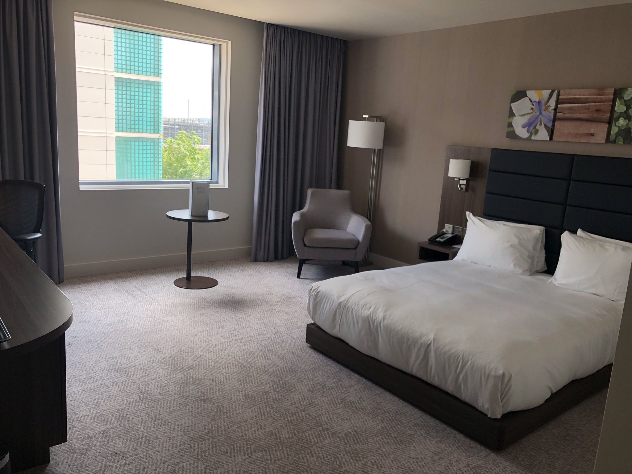 A hotel room with a bed, a chair, a desk, a lamp, and a window with curtains.