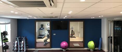 A gym with exercise equipment, a treadmill, and a mirrored wall.