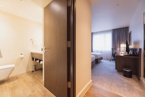 Comfortable room with a large bed, desk, and bathroom featuring a toilet, sink, and trash bin.