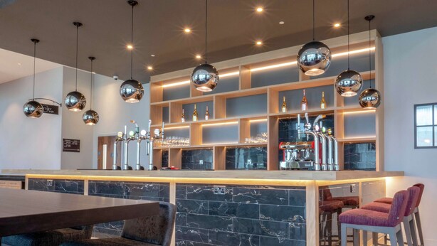 Un espace bar moderne doté d’un comptoir en marbre, de plusieurs tabourets et d’une machine à café.
