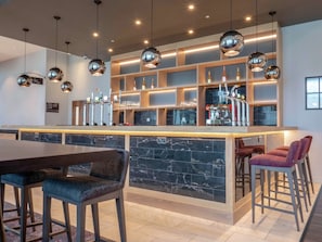 A modern bar area with a marble countertop, multiple bar stools, and a coffee machine.