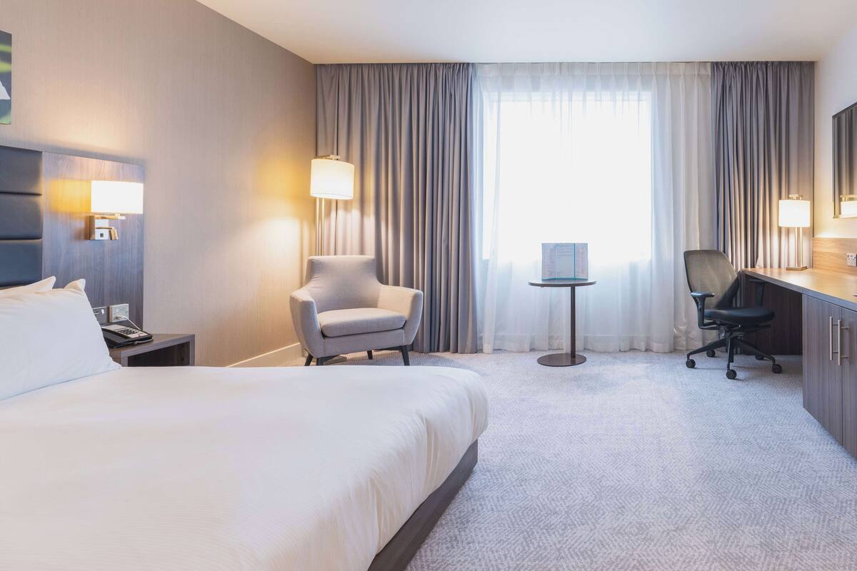 A hotel room with a large bed, two chairs, a desk, and a small table.