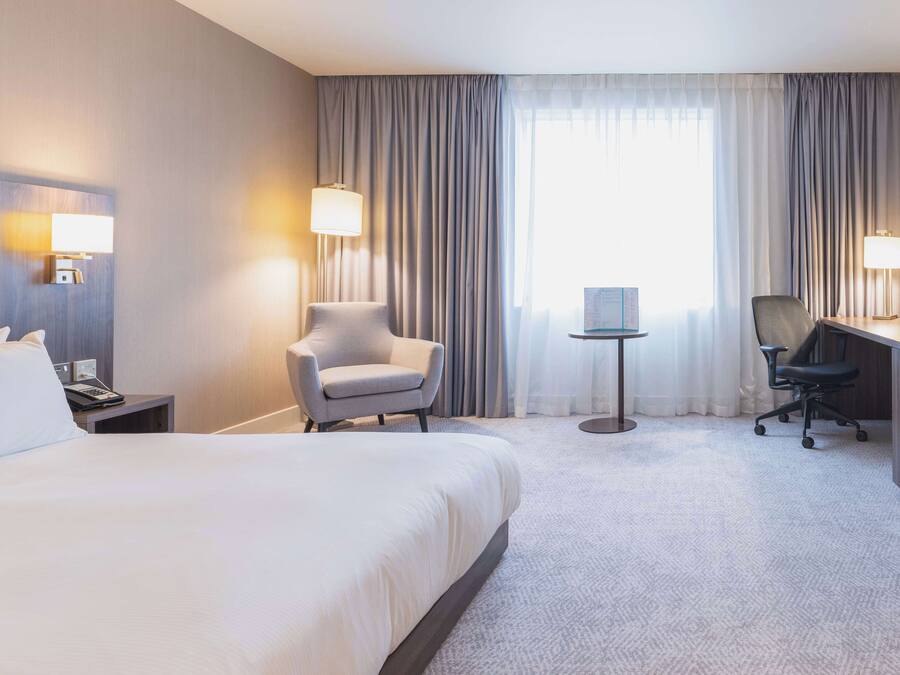 A hotel room with a large bed, two chairs, a desk, and a small table.