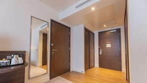 Un couloir d’hôtel avec un plancher en bois, un comptoir de réception sur lequel se trouve un plateau d’articles divers, et deux portes en bois.