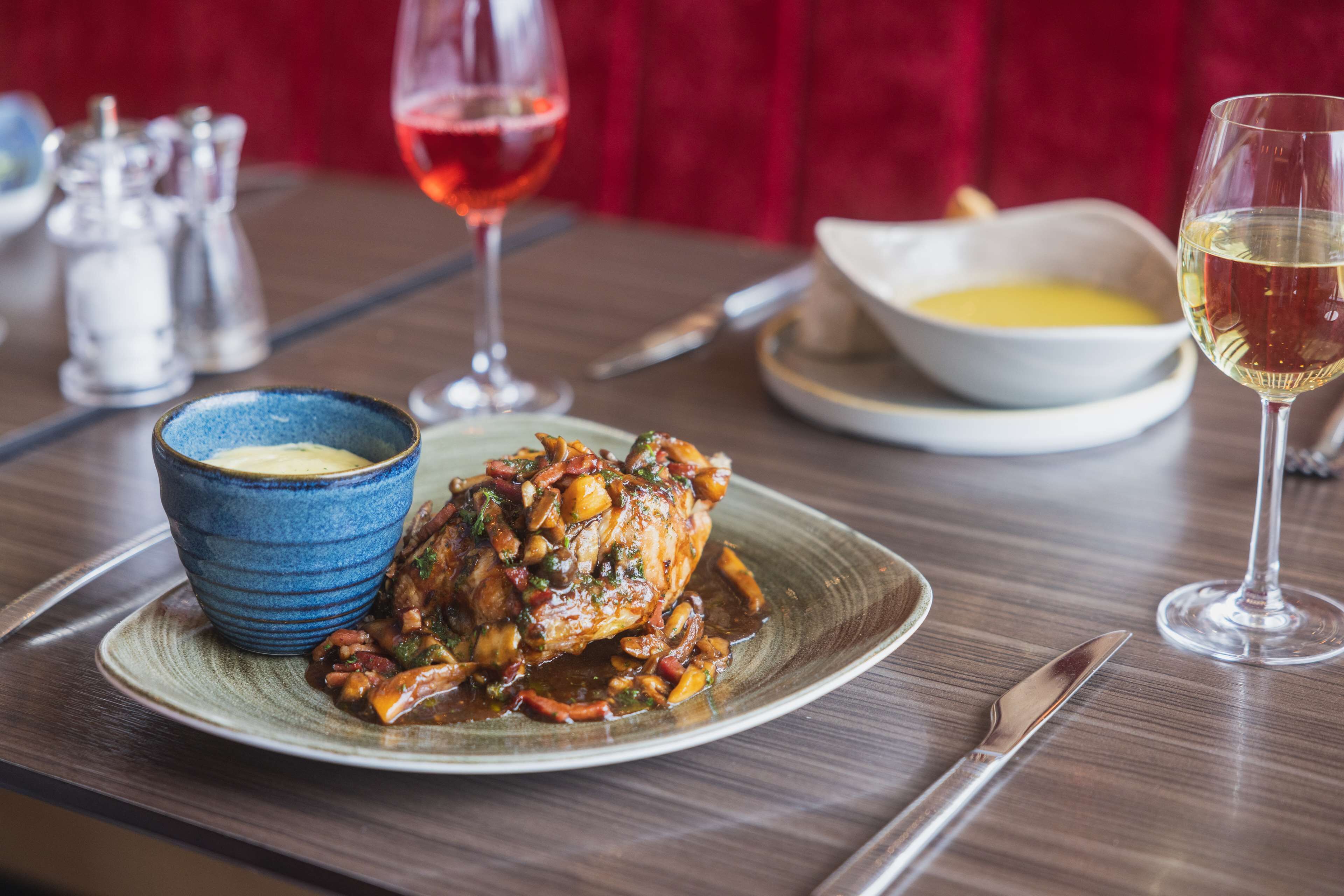 A dining table with a plate of food, a bowl of soup, and two glasses of wine.
