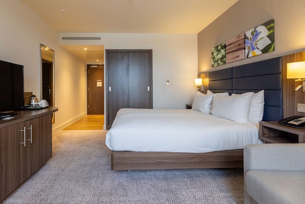 A hotel room with a large bed, a TV, a desk, and a cabinet.