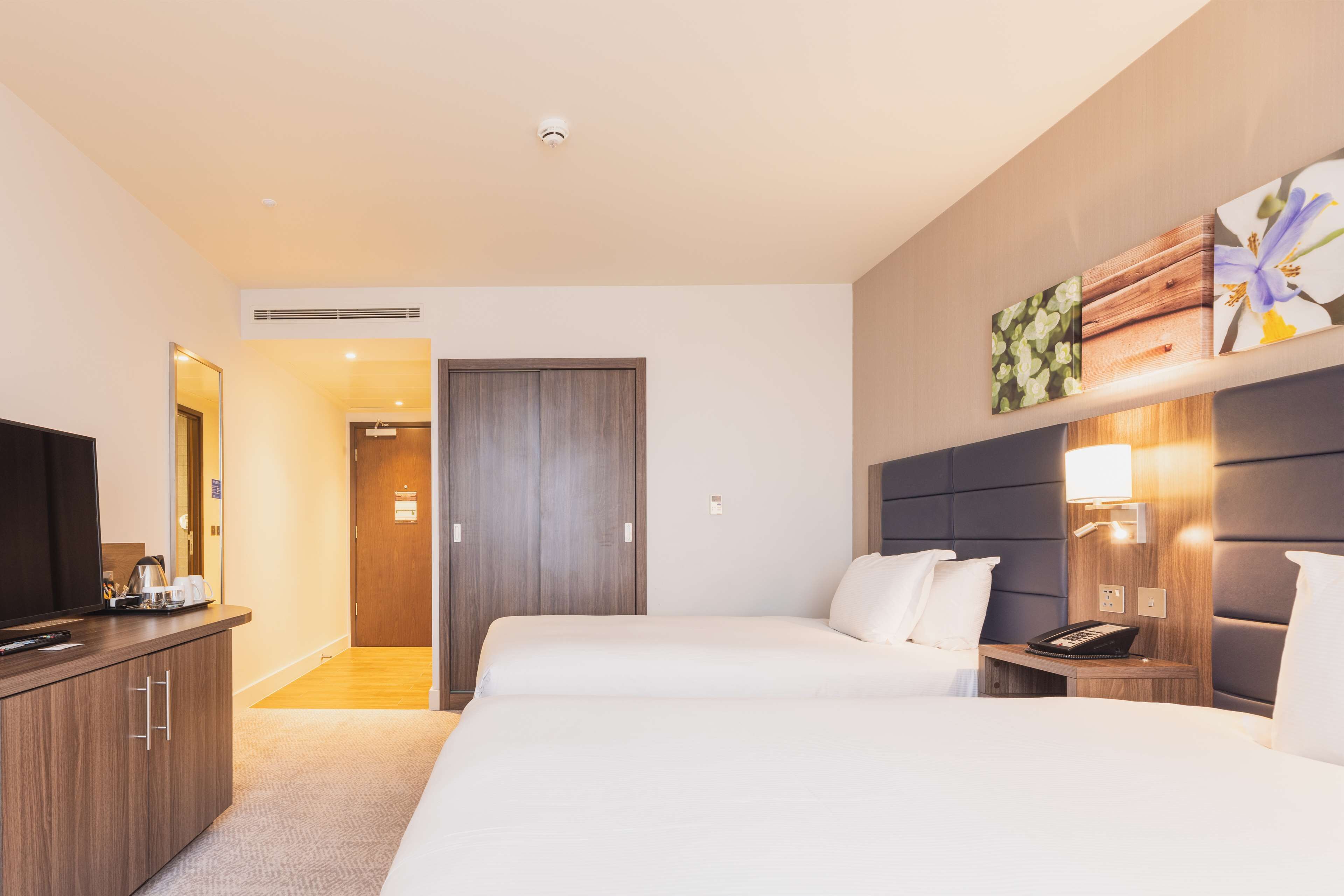 A hotel room with a large bed, a desk with a telephone, a TV, and a wardrobe.