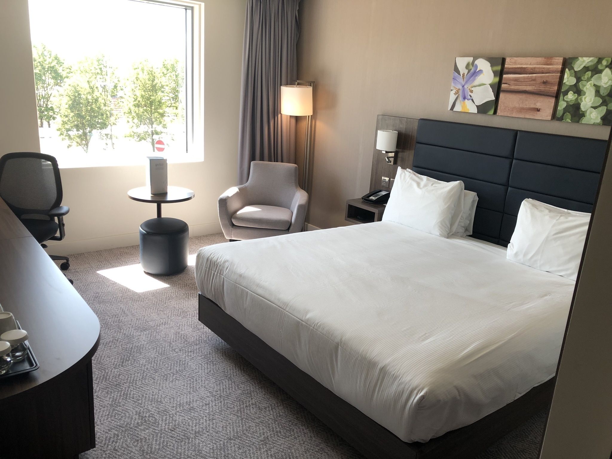 A hotel room with a large bed, a desk, a chair, a small table, and a lamp.