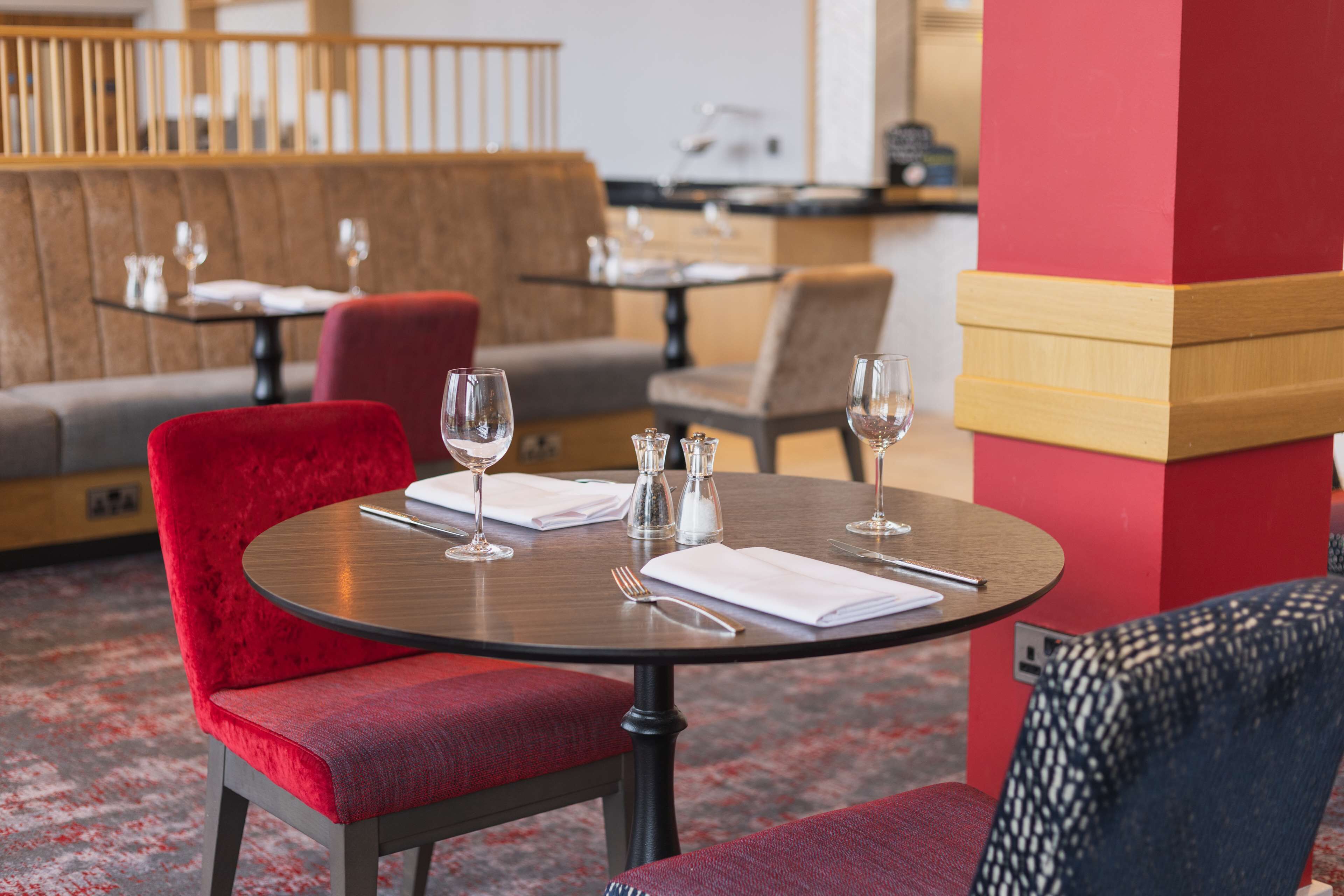 A dining area with round tables, red upholstered chairs, and a red pillar.