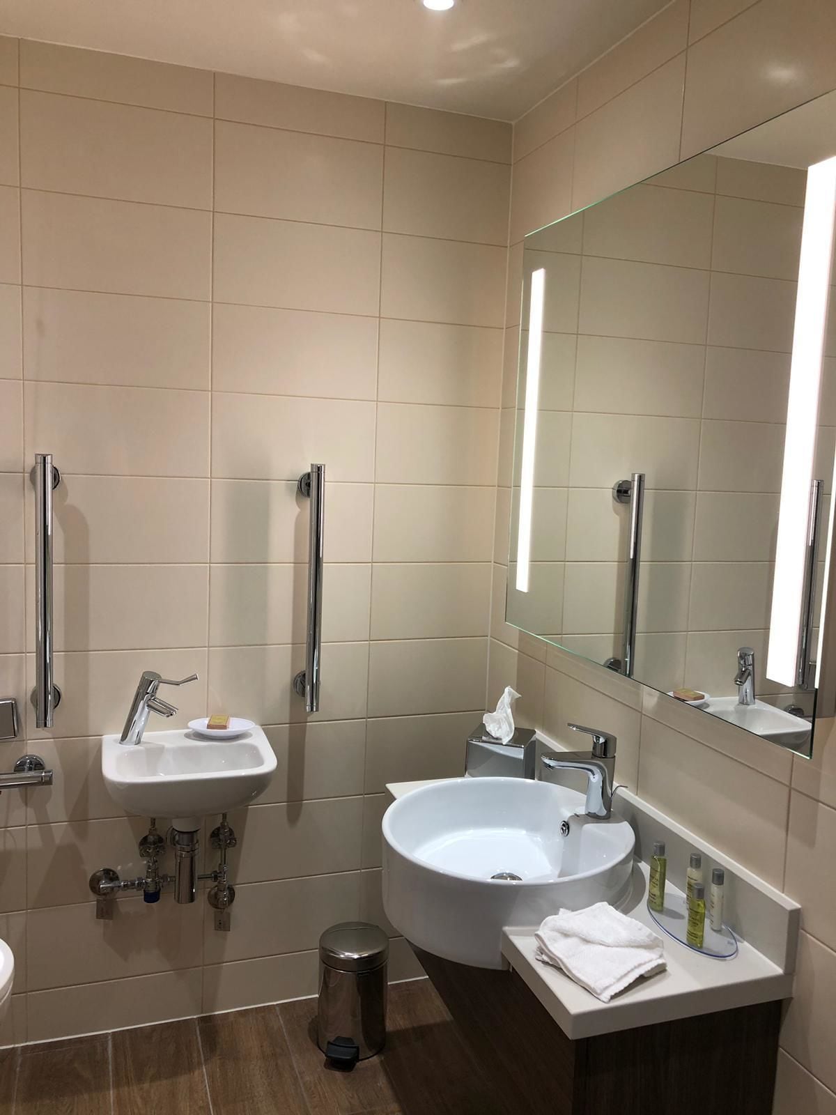 Un baño moderno con dos lavamanos, un espejo grande y un mueble tocador con artículos de aseo.
