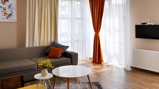 A modern living room with a grey sofa, a round coffee table, and a TV mounted on the wall. - BFG Suites Apartments (Tbilisi)