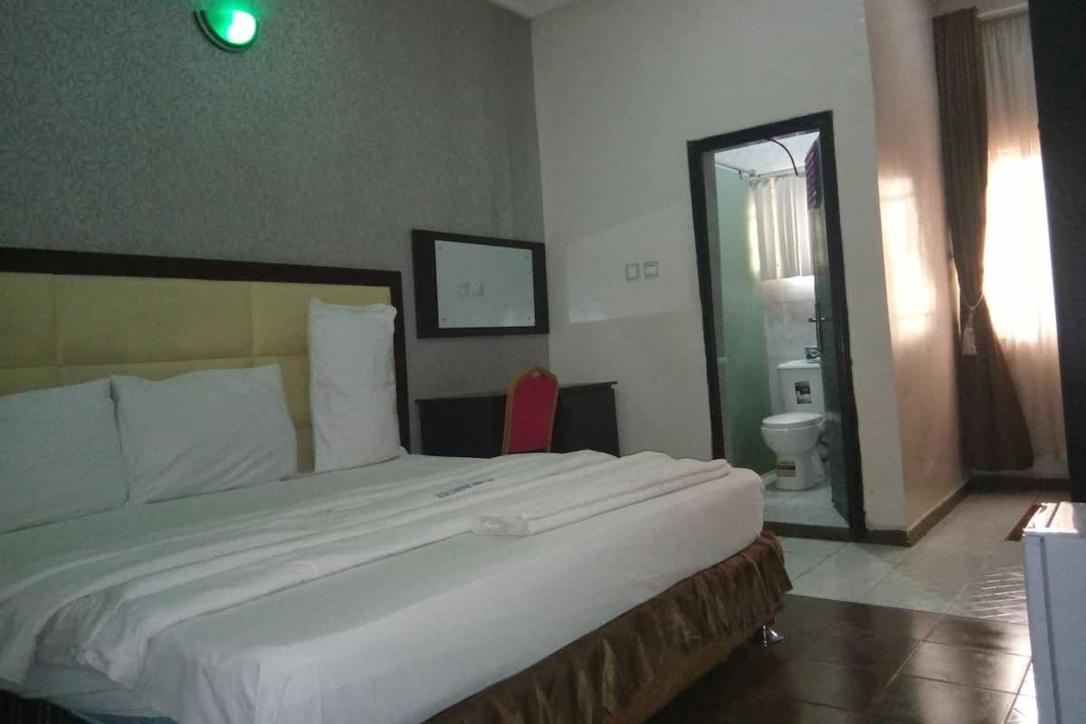 A hotel room with a large bed, a bedside table, a mirror, and a toilet visible through an open door.