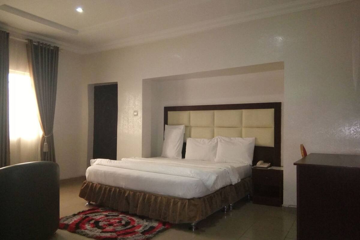 A hotel room with a bed, bedside table, chair, and a rug.
