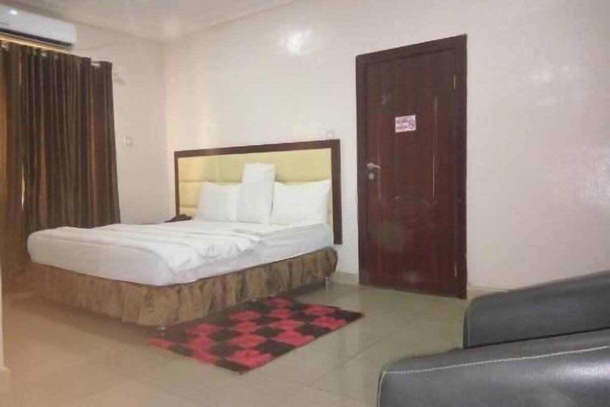 A bedroom with a bed, a dark wooden door, and a tiled floor.